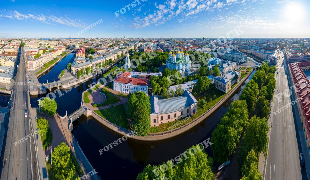 Фотография панорамы Санкт-Петербурга с высоты, открывающая вид на улицы центра города, Никольский морской собор, Крюков канал и реку Неву. Снимок передает атмосферу исторического Петербурга, где архитектура прошлых веков гармонично сочетается с водными каналами и мостами города. Панорамный ракурс позволяет увидеть масштабы улиц, городские мосты и архитектурные детали зданий, подчеркивая красоту северной столицы России. Изображение идеально подходит для туристических публикаций, постеров, архитектурных проектов, интерьерного оформления и коллекций фотографий Петербурга.